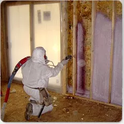 Technician in hazmat suit, applying spray foam insulation in a wall.