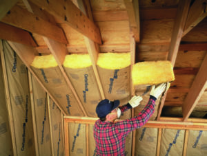 Fiberglass batt insulation being installed in an attic ceiling by a technician in a red plaid shirt.