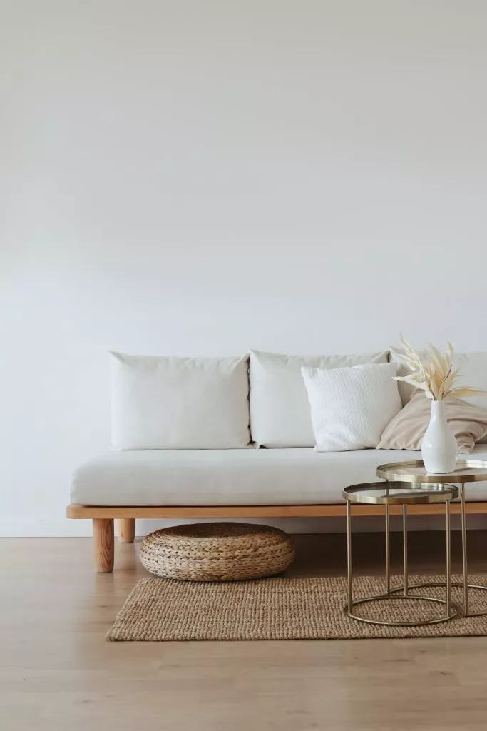 White couch against white drywall. Light wood floors, and small metal table in front of couch.