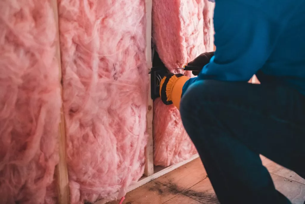 A technician cutting fiberglass batts so they fit in a wall